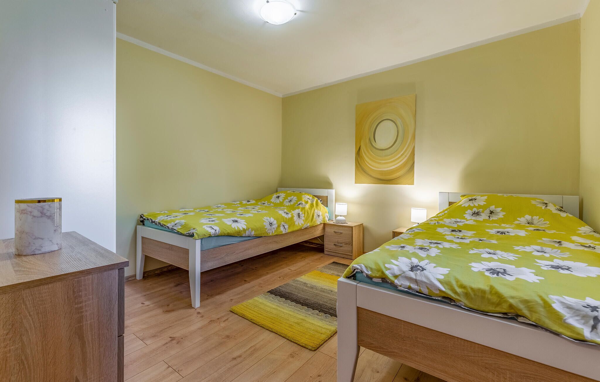 A room with two single beds, wooden flooring, a small desk, and a yellow rug.