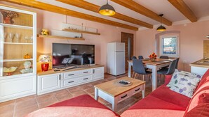 A cozy living room with a TV, sofa, and coffee table. There's a dining area with chairs and a table.