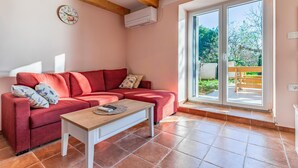 A red sofa with a wooden coffee table, a wall clock, and a large sliding glass door to a garden.