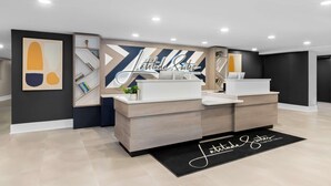 A modern hotel lobby with a reception desk, a large abstract artwork, and a wall with the hotel's name. - Latitude Suites Tinton Falls Eatontown Bw Premier (Tinton Falls)