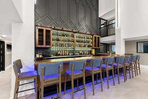 Un espace bar doté d’un long comptoir, de plusieurs étagères remplies de bouteilles et de plusieurs chaises avec des coussins bleus.
