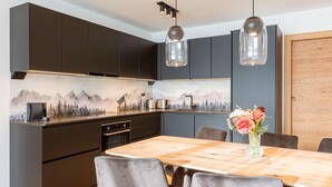 A modern kitchen with dark cabinets, a wooden dining table, and a vase of flowers. - Exclusive Apartment in Fiss (Fiss)