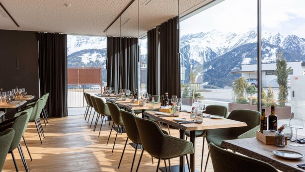 A dining area with tables set for a meal, large windows with a mountain view, and a modern interior design. - Exclusive Apartment in Fiss (Fiss)