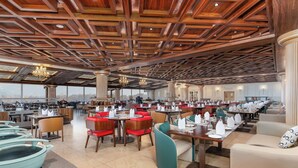 A spacious restaurant with high ceilings, wooden beams, and modern lighting. Tables are set with white tablecloths and red chairs. - Sarovar Premiere Srinagar (Srinagar)