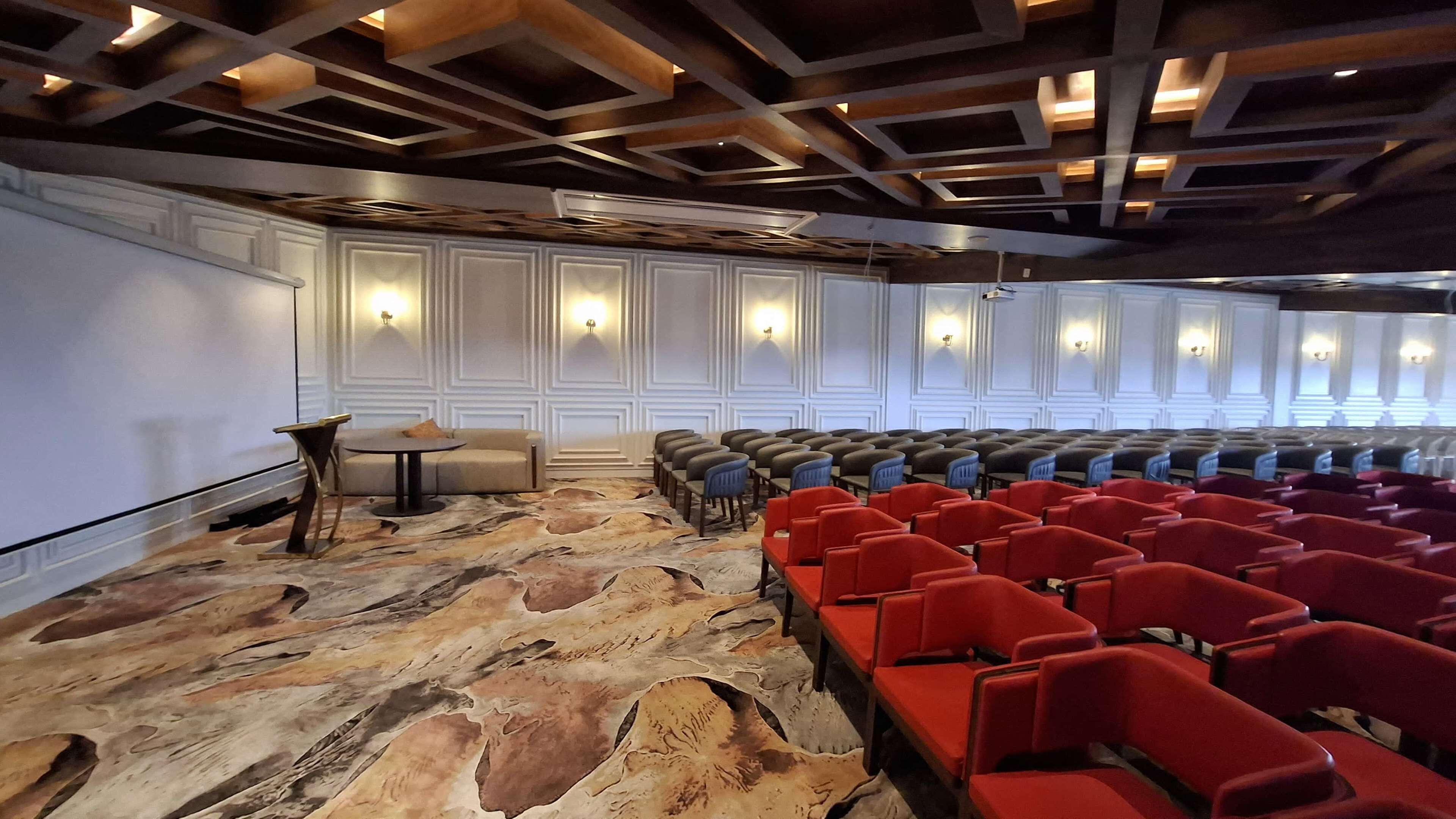A conference room with a patterned carpet, rows of red chairs, a sofa, and a small table.