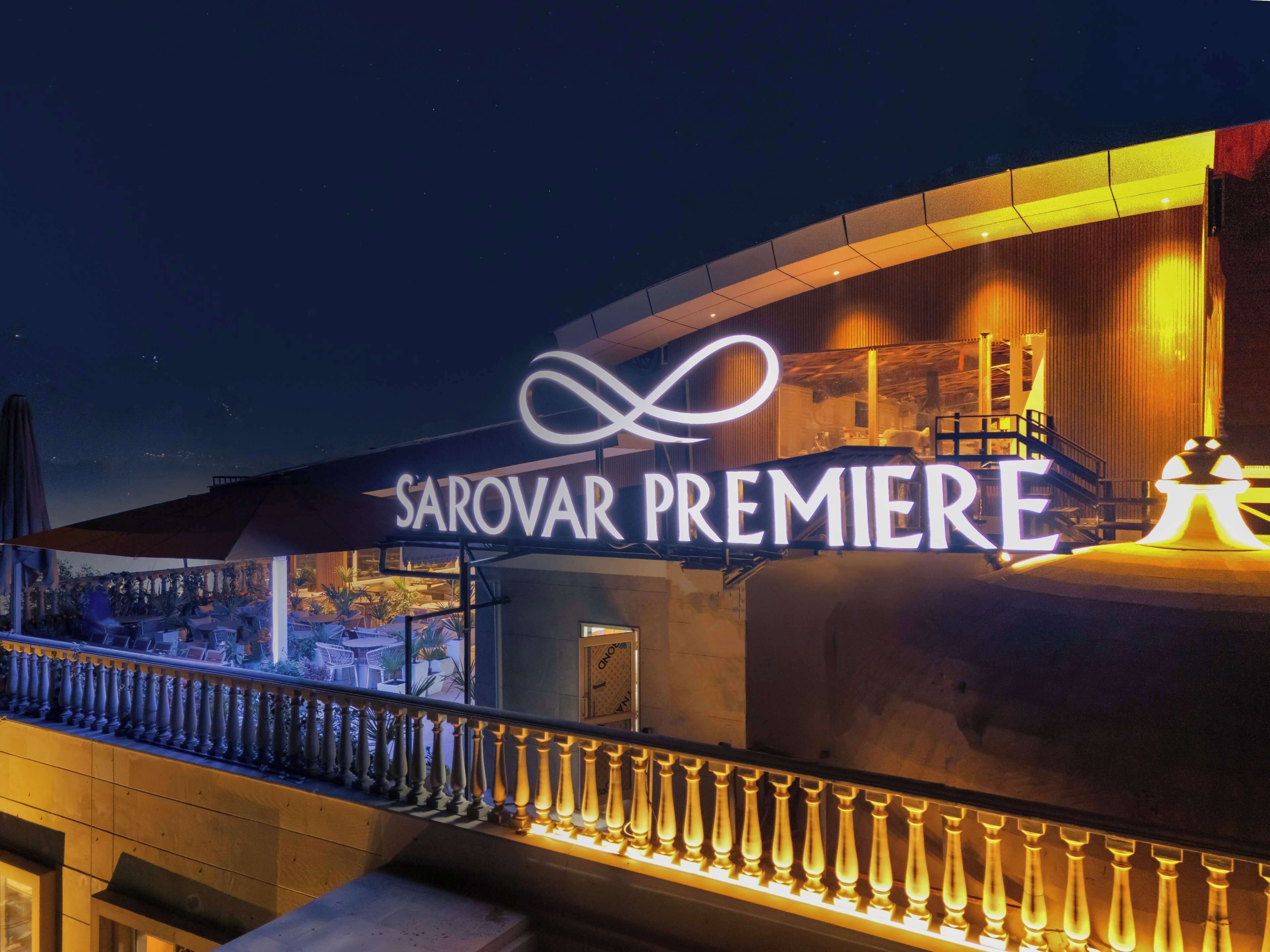 Exterior de un hotel con un llamativo letrero 'SAROVAR PREMIERE', un balcón con barandilla y vistas de la ciudad.