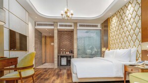 A hotel room with a bed, a desk, a chair, a minibar, and a view of the city. - Sarovar Premiere Srinagar (Srinagar)