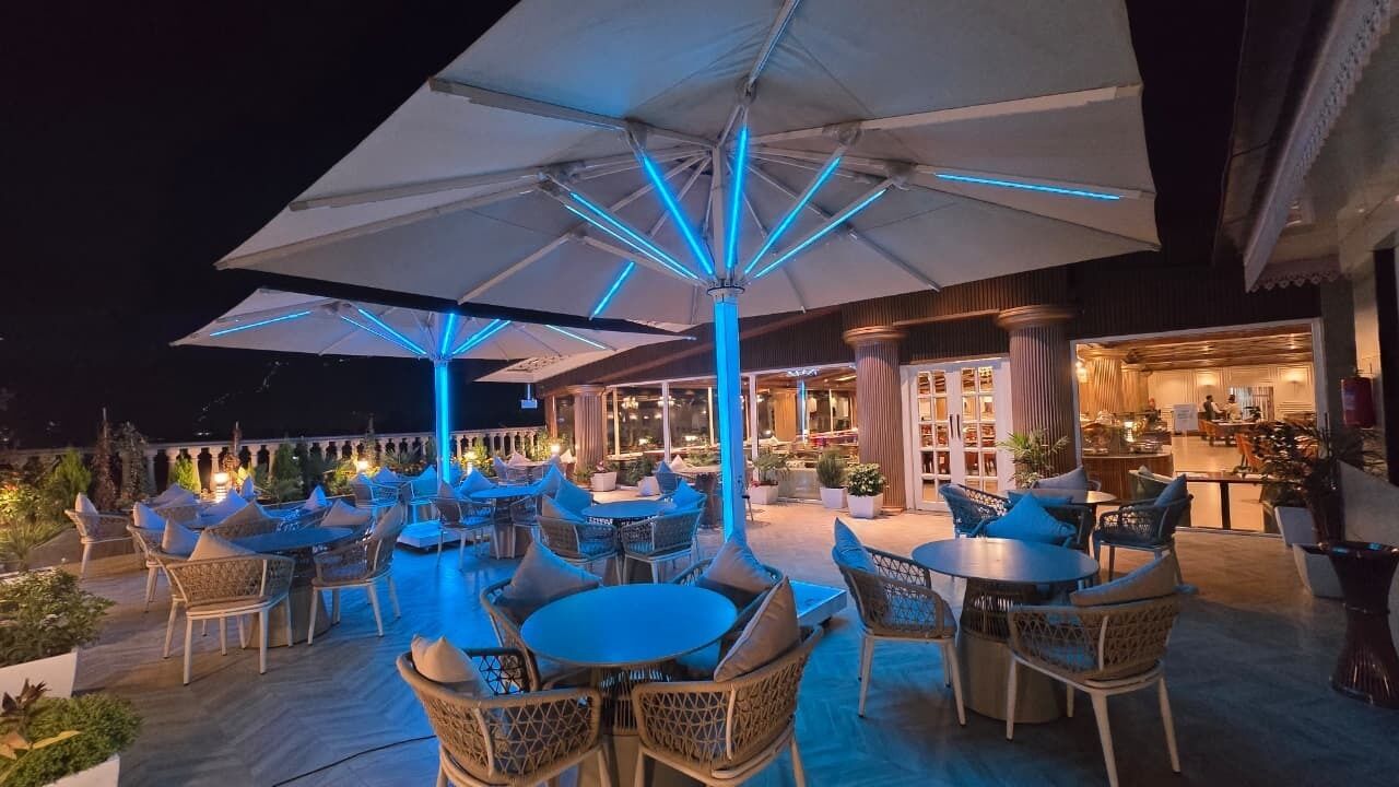 An outdoor patio area with round tables and chairs, umbrellas, and potted plants.