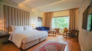 A hotel room with a large bed, a desk, a chair, a sofa, and a window with curtains.