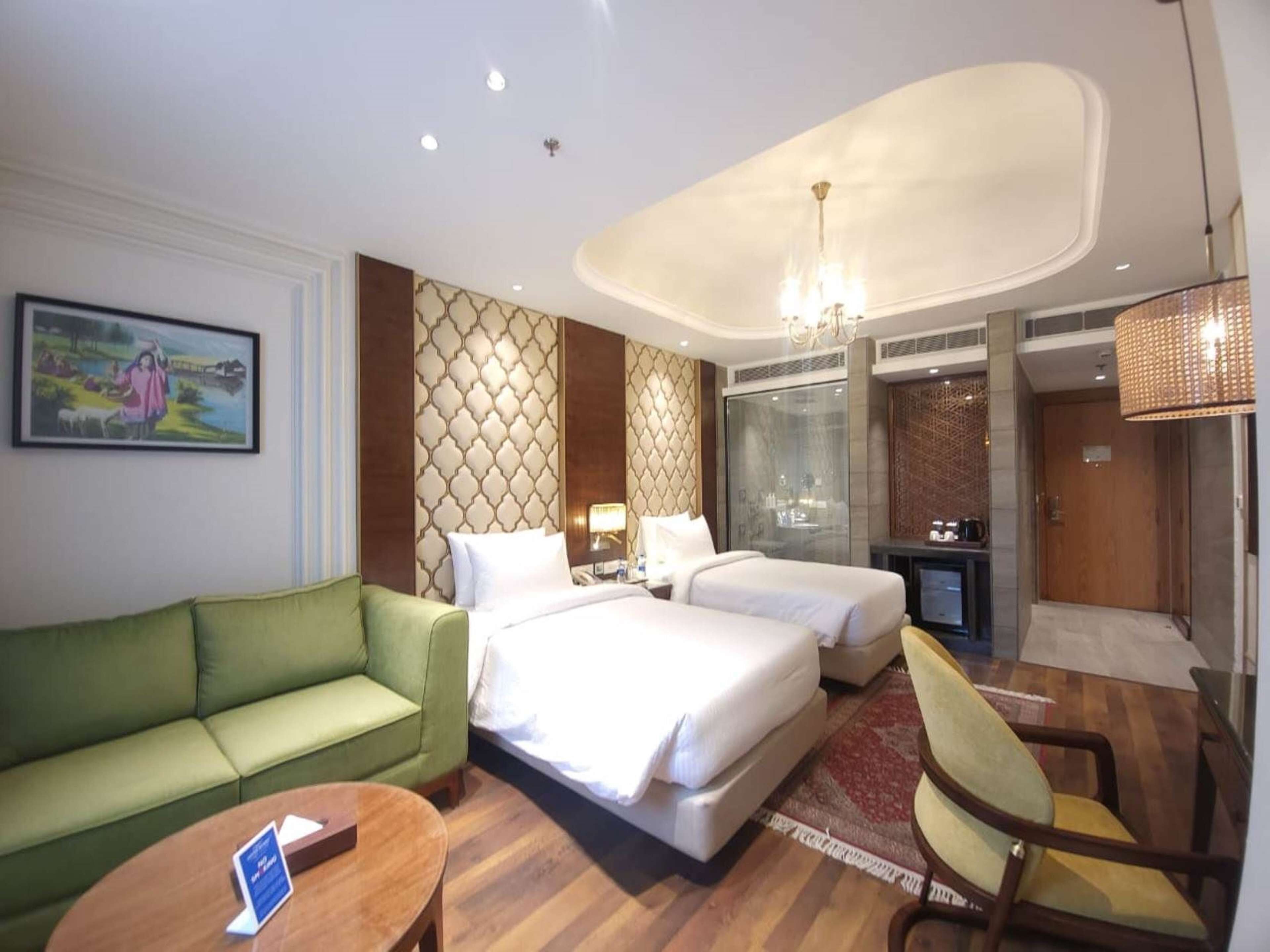 A hotel room with two beds, a green sofa, a wooden coffee table, and a painting on the wall.