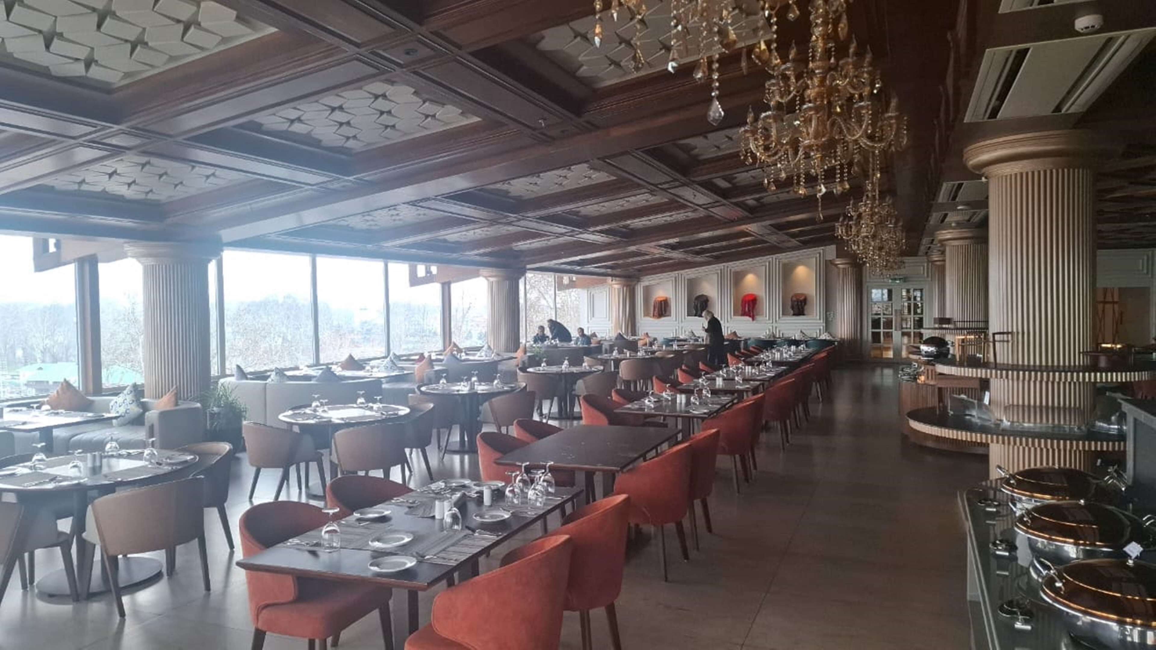 A spacious dining area with long tables, red chairs, and a high ceiling with decorative elements.