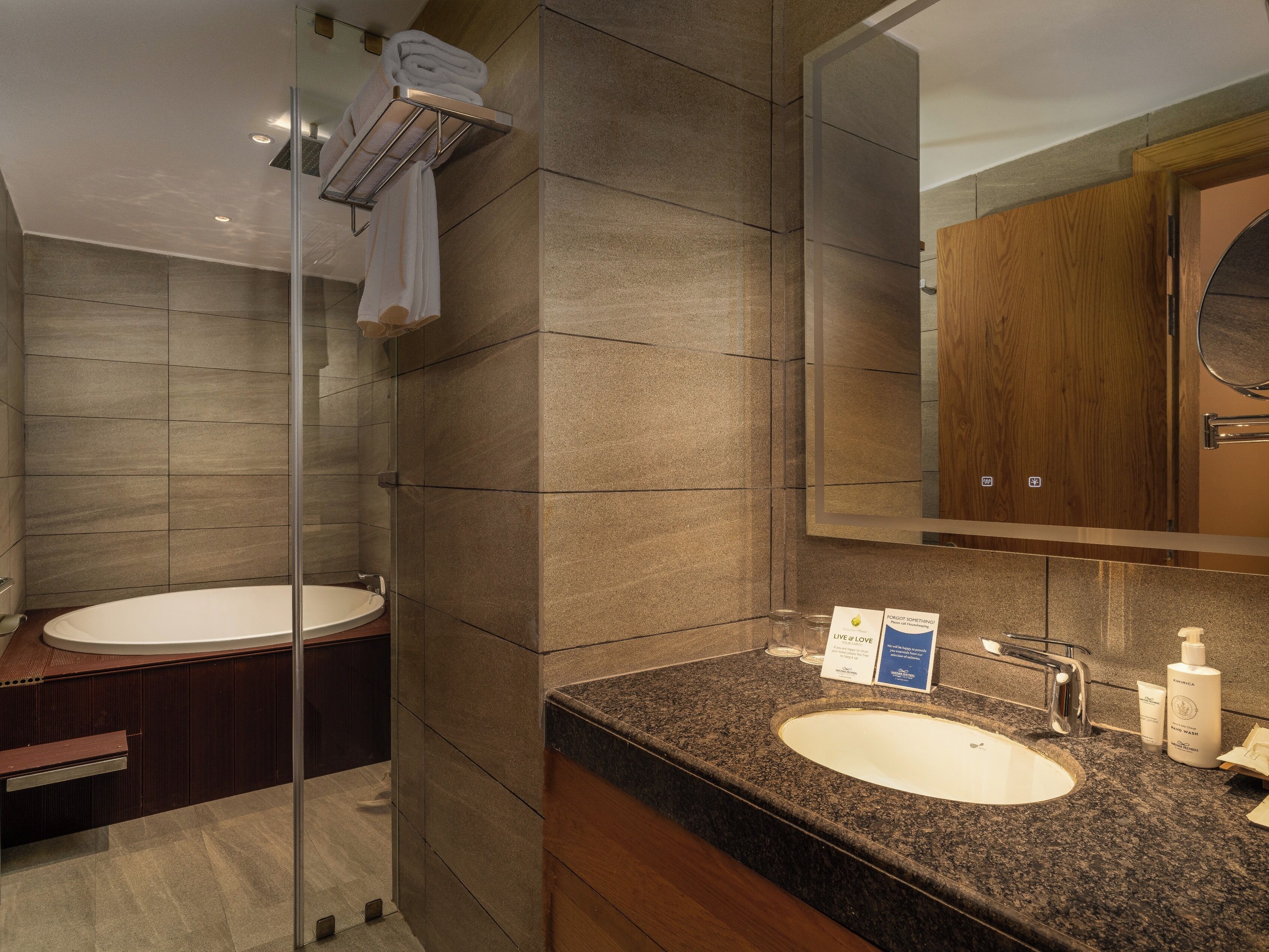 A modern bathroom with a glass-enclosed shower, a freestanding bathtub, and a granite countertop sink with toiletries.