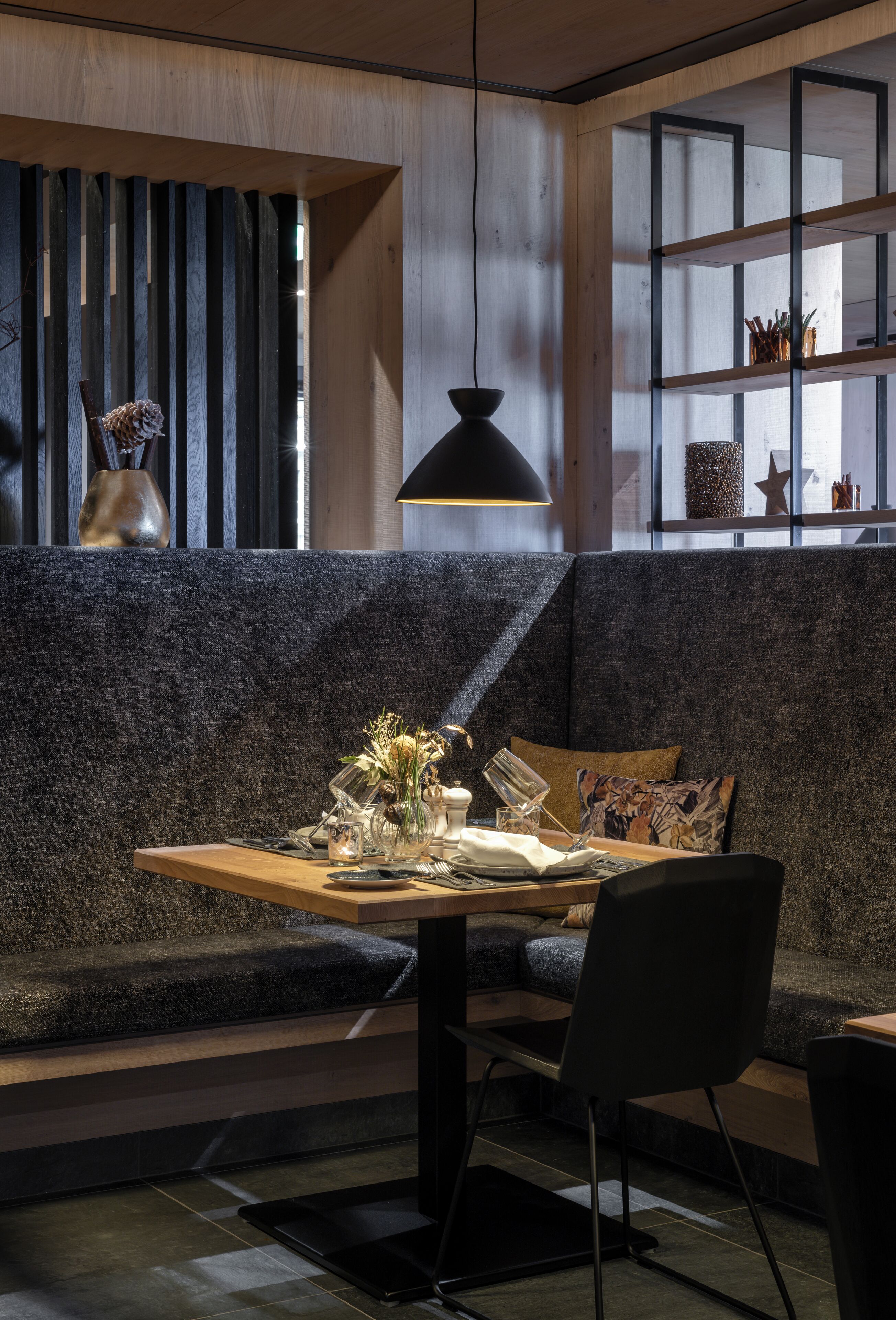 A modern interior with a wooden table, black chair, and a grey cushioned bench.