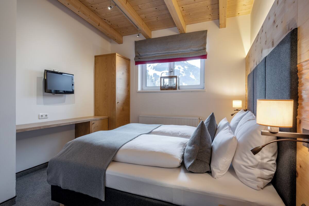 A bedroom with a bed, a TV, a window with a view of mountains, and a lamp.
