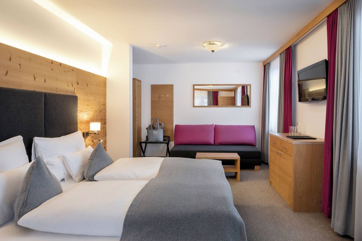 A modern hotel room with a large bed, a sofa, a desk, and a TV.