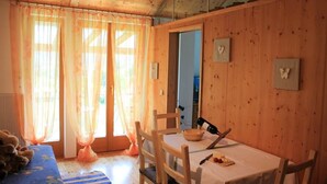 L’intérieur d’un chalet en bois, avec une table à manger, des chaises, un ours en peluche et une fenêtre ornée de rideaux légers.