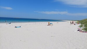 Un'ampia spiaggia sabbiosa con acque cristalline, alcune persone e ombrelloni da spiaggia.