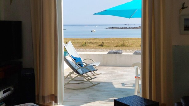 Una stanza con vista sul mare, una sedia da spiaggia, un tavolo e un ombrellone blu.