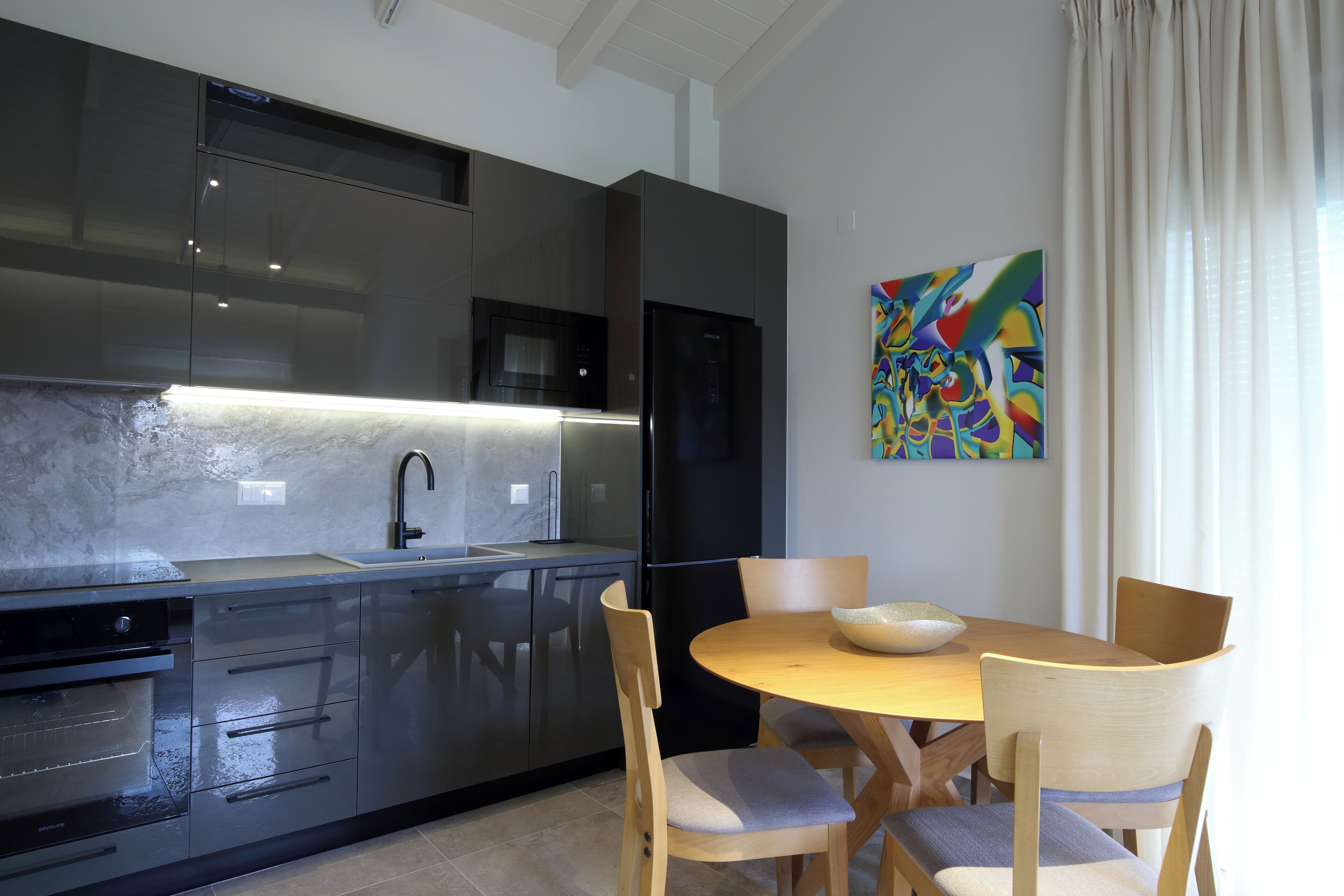 Una cucina moderna con forno integrato, un frigorifero nero e un tavolo da pranzo in legno con sedie.