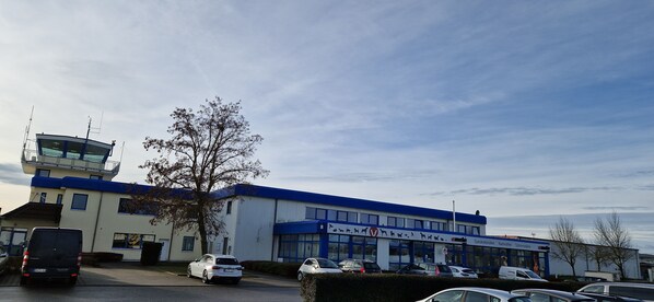 Un bâtiment à la façade bleue et blanche, un parking avec plusieurs voitures et un arbre au premier plan.