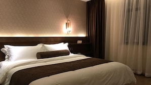 A hotel room with a large bed, a nightstand, a wall-mounted lamp, and sheer curtains.