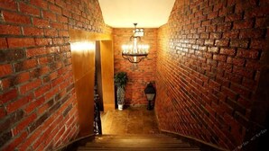 A narrow brick-walled hallway with a wooden staircase, a chandelier, and a potted plant.
