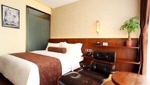 A hotel room with a bed, a desk, a chair, a potted plant, and a wall-mounted shelf. - James Joyce Coffetel (Beijing)