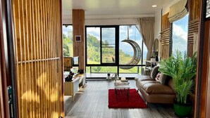 A spacious living room with a large window, a red rug, a sofa, and a hanging moon lamp. - Bella Lunar Villa (Mae Fa Luang)