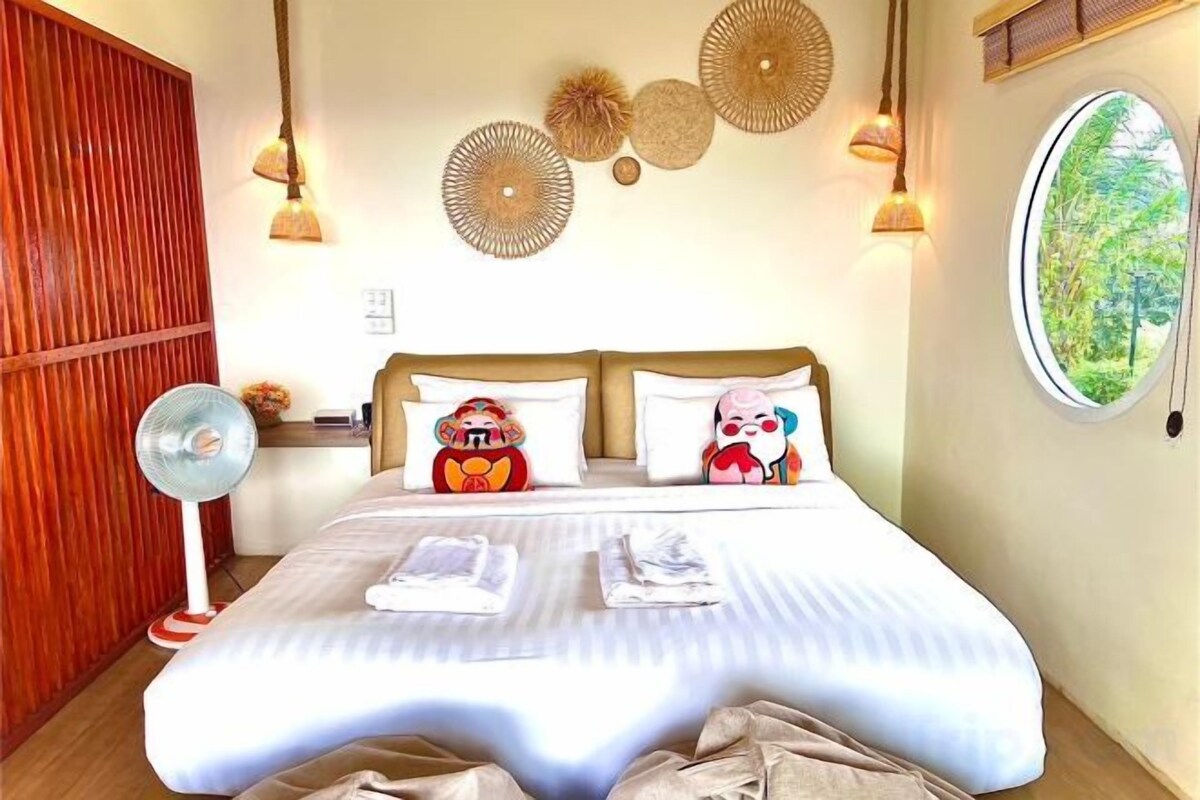 A hotel room with a bed, pillows, a fan, and a window.