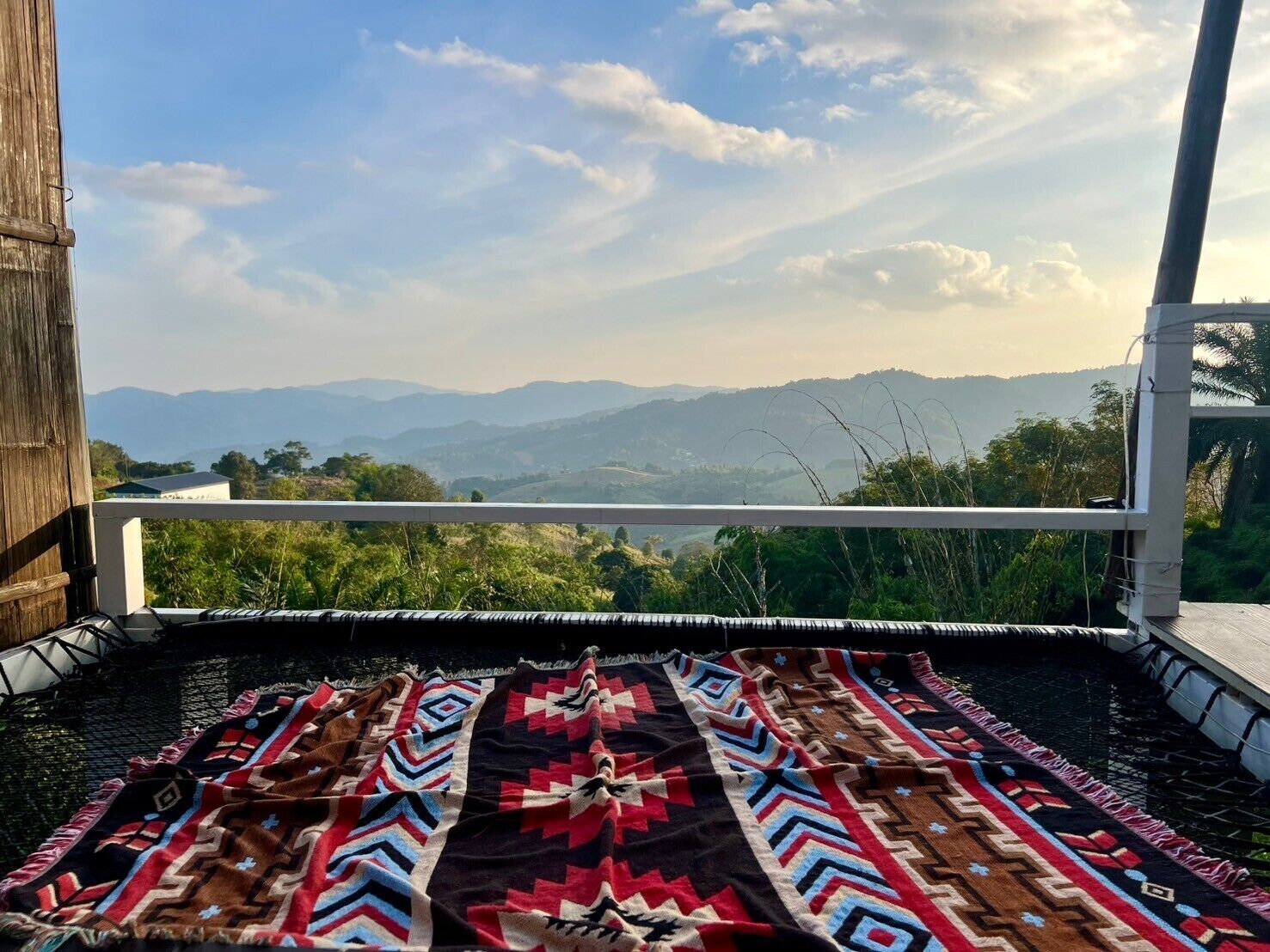 A balcony with a patterned rug, overlooking a mountainous landscape.
