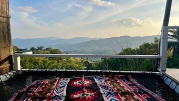 A balcony with a patterned rug, overlooking a mountainous landscape.