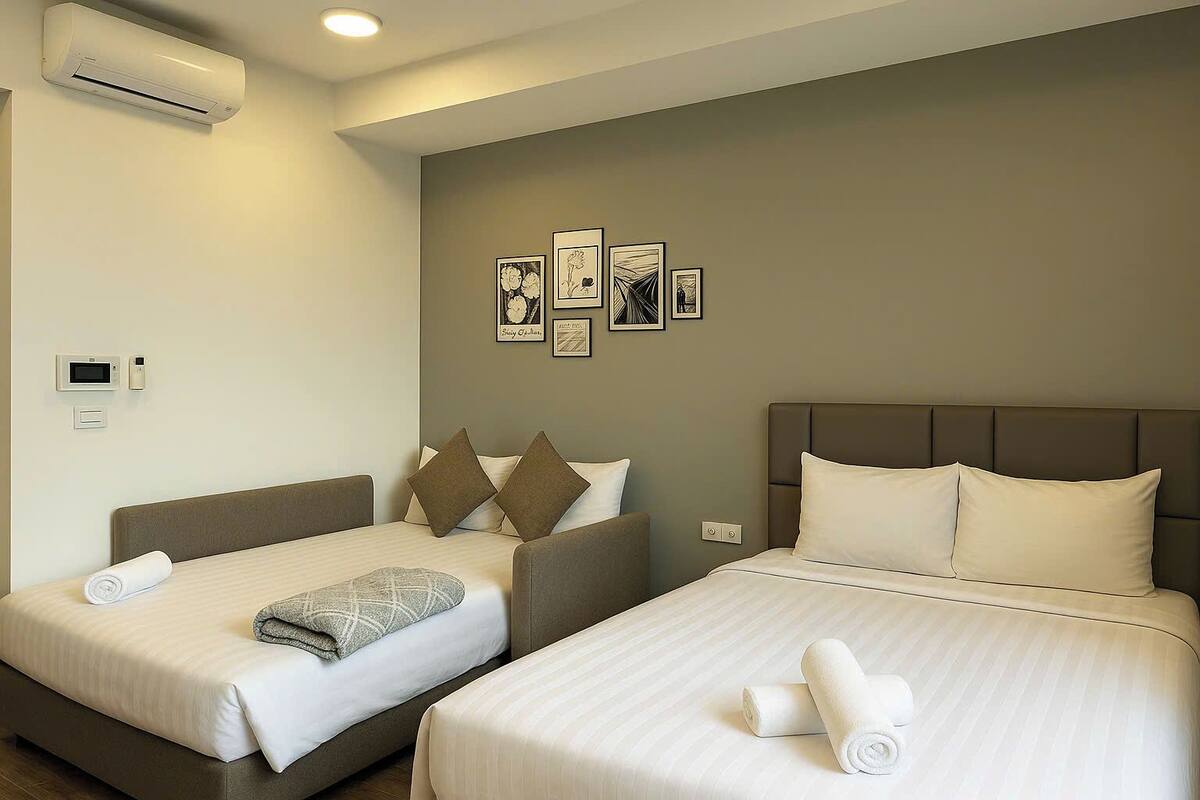 A hotel room with two beds, a wall-mounted air conditioner, a microwave, and a thermostat.