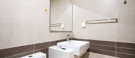 Un baño moderno con un lavamanos blanco, un espejo y un inodoro.