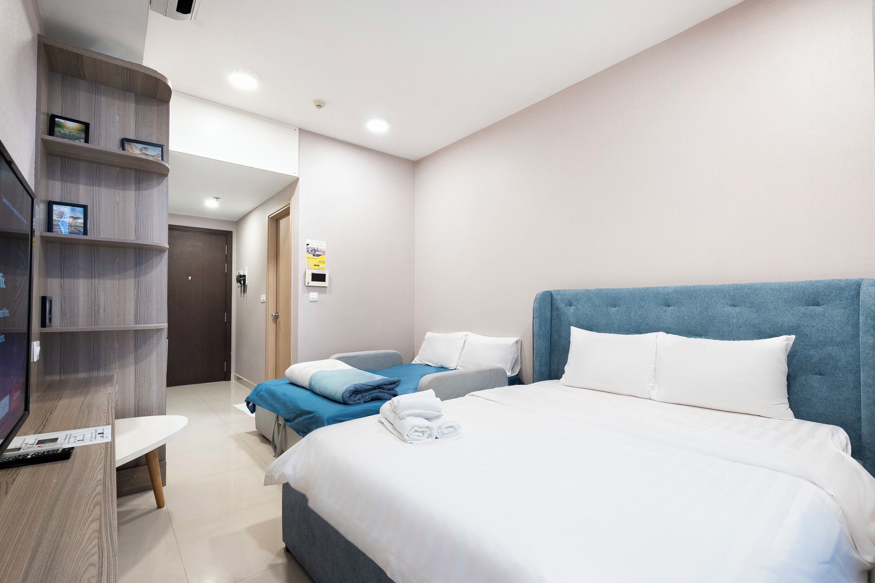 A hotel room with a large bed, a smaller bed, a desk with a TV, and a wardrobe.