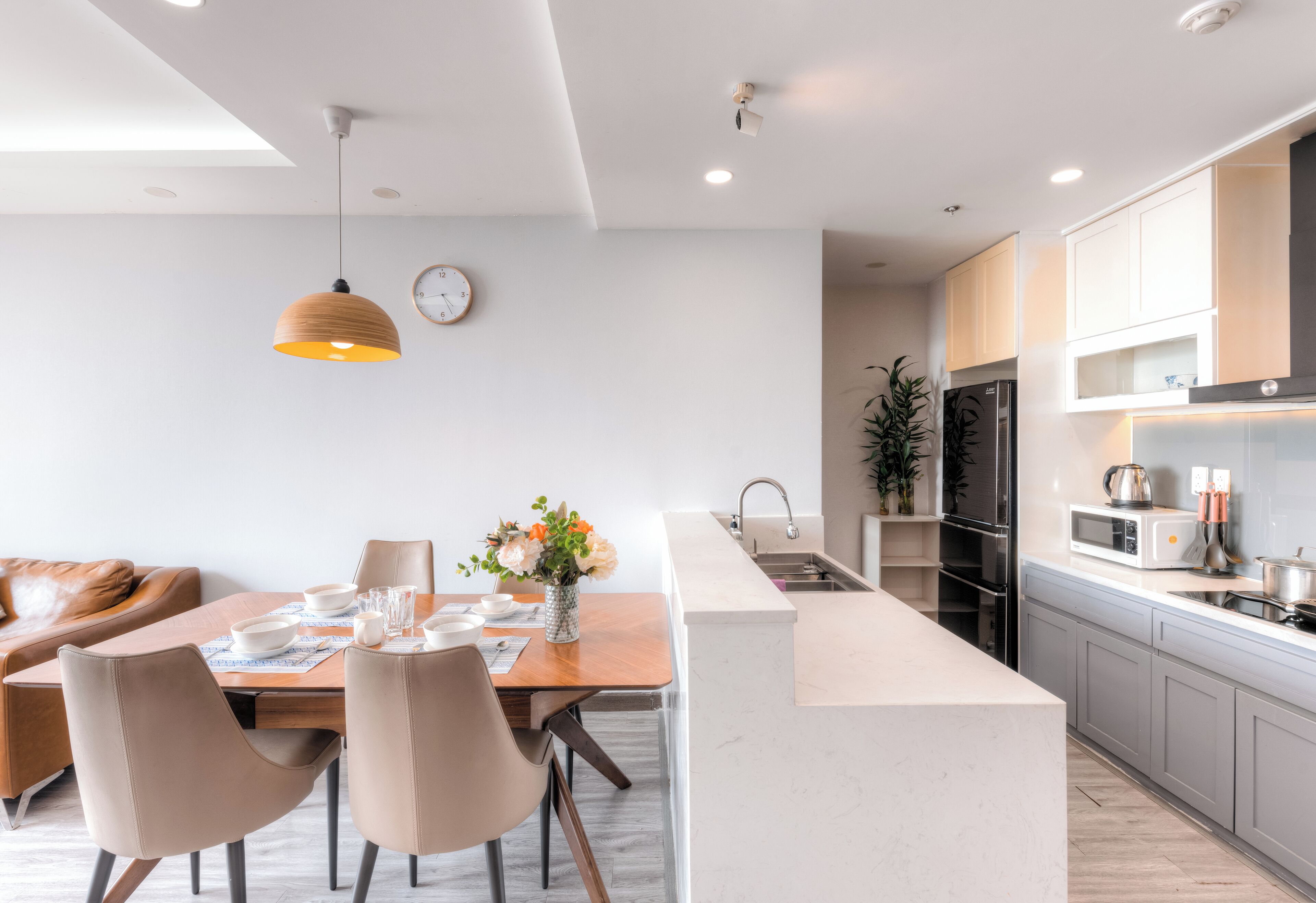 A modern kitchen with a central island, a dining area with chairs and a table, and a clock on the wall.