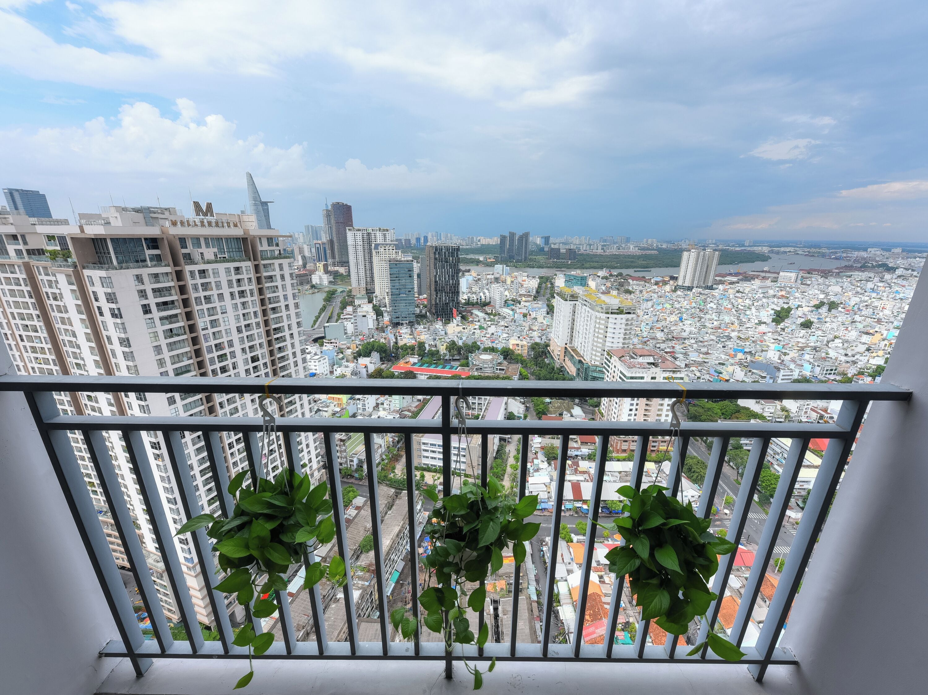 Une vue sur la ville, prise depuis un balcon doté de rampes en métal et de plantes en pot.