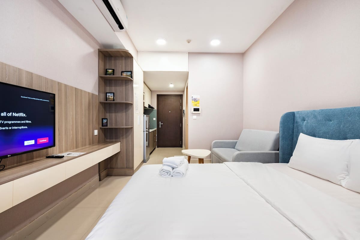 A hotel room with a bed, a TV on a wooden shelf, a sofa, and a small table.