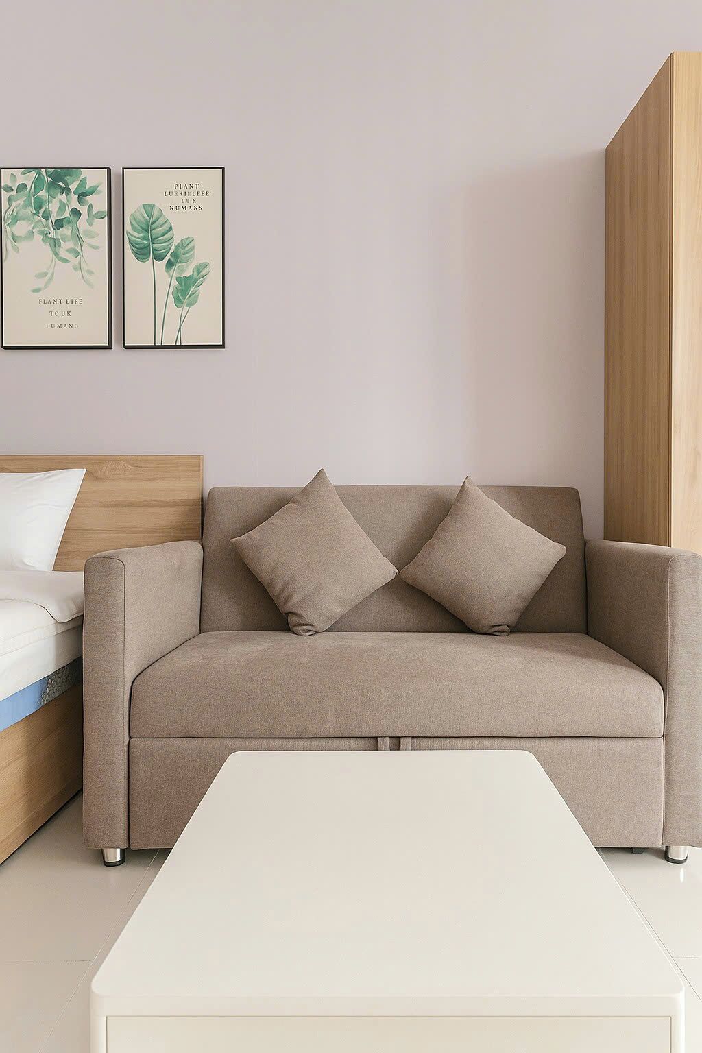 Una habitación en tonos neutros con un sofá, una mesa de centro blanca y dos láminas botánicas enmarcadas en la pared.