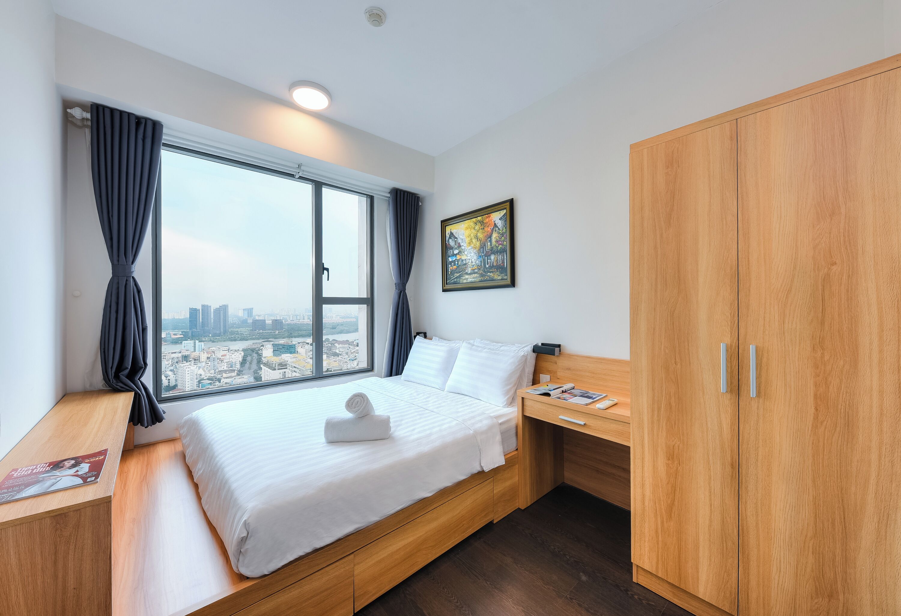 Une chambre d’hôtel moderne avec un grand lit, un bureau en bois, une armoire et une vue sur la ville.