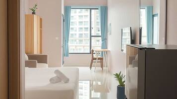 A modern hotel room with a bed, a dining area, a refrigerator, and a large window with curtains.
