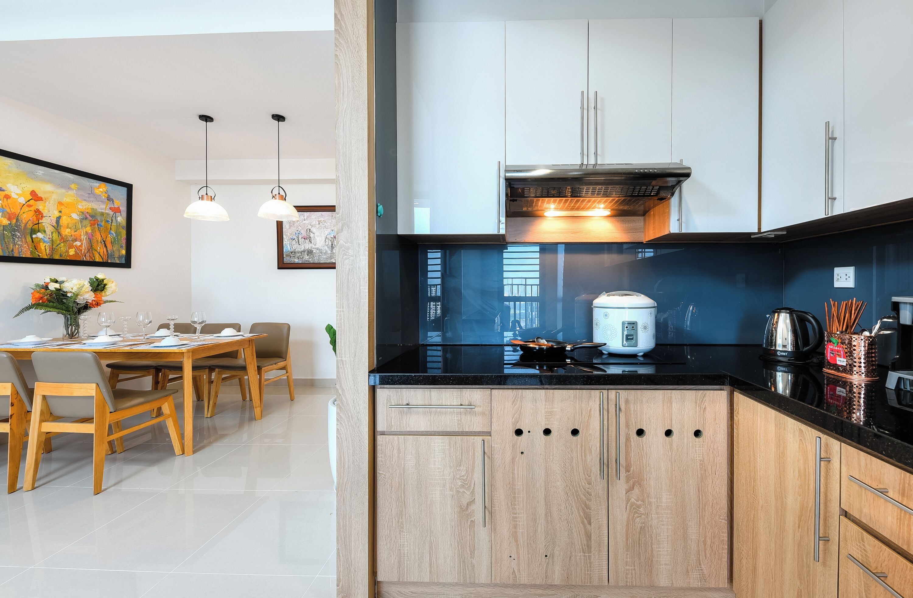 Una cocina moderna con armarios de madera, encimera negra y comedor con mesa y sillas.
