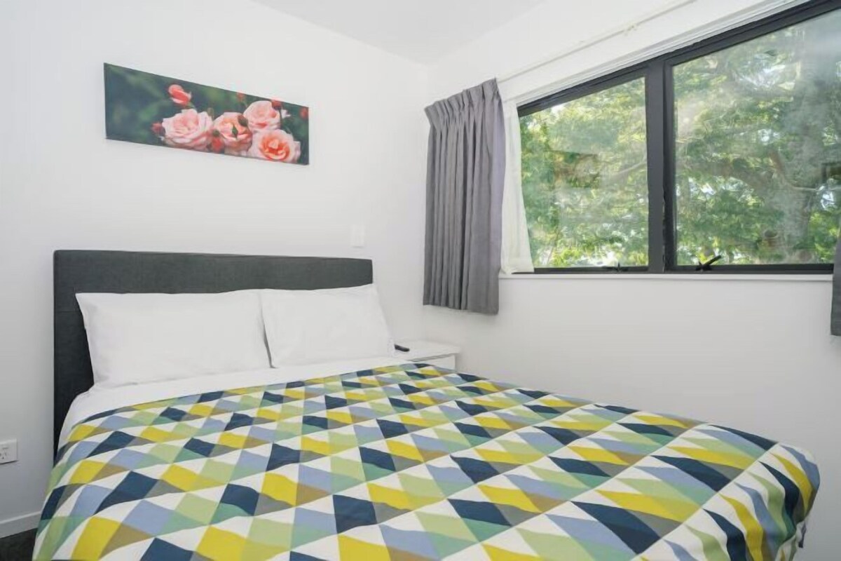 Un dormitorio con una cama, una ventana con cortinas y un cuadro con motivos florales en la pared.