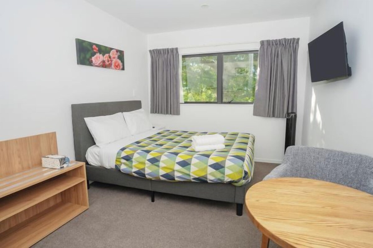 A hotel room with a bed, a wooden side table, a gray sofa, and a TV mounted on the wall.