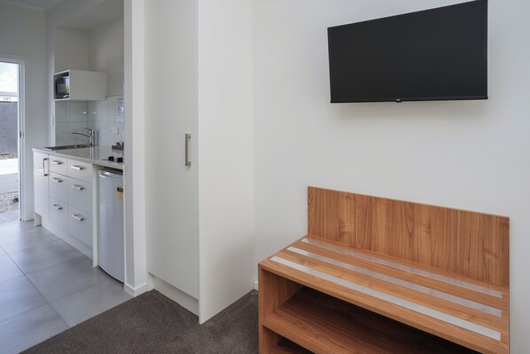 A modern kitchen with white cabinets, a microwave, and a wooden bench. - Yates Park Motel (Auckland)