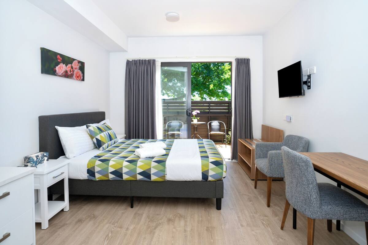 A modern bedroom with a bed, bedside table, and a desk with chairs.