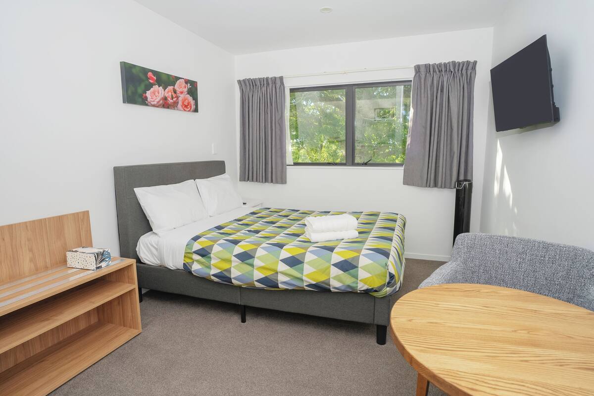 A modern hotel room with a bed, a desk, a chair, and a TV.