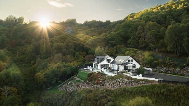 Une maison moderne dotée d’une grande terrasse et offrant une vue sur une colline boisée.