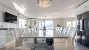 Une cuisine moderne avec une grande table à manger, des chaises blanches et un réfrigérateur en acier inoxydable.