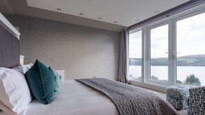 Une chambre dotée d’un grand lit, offrant une vue sur un lac, et présentant un design moderne au niveau du plafond.