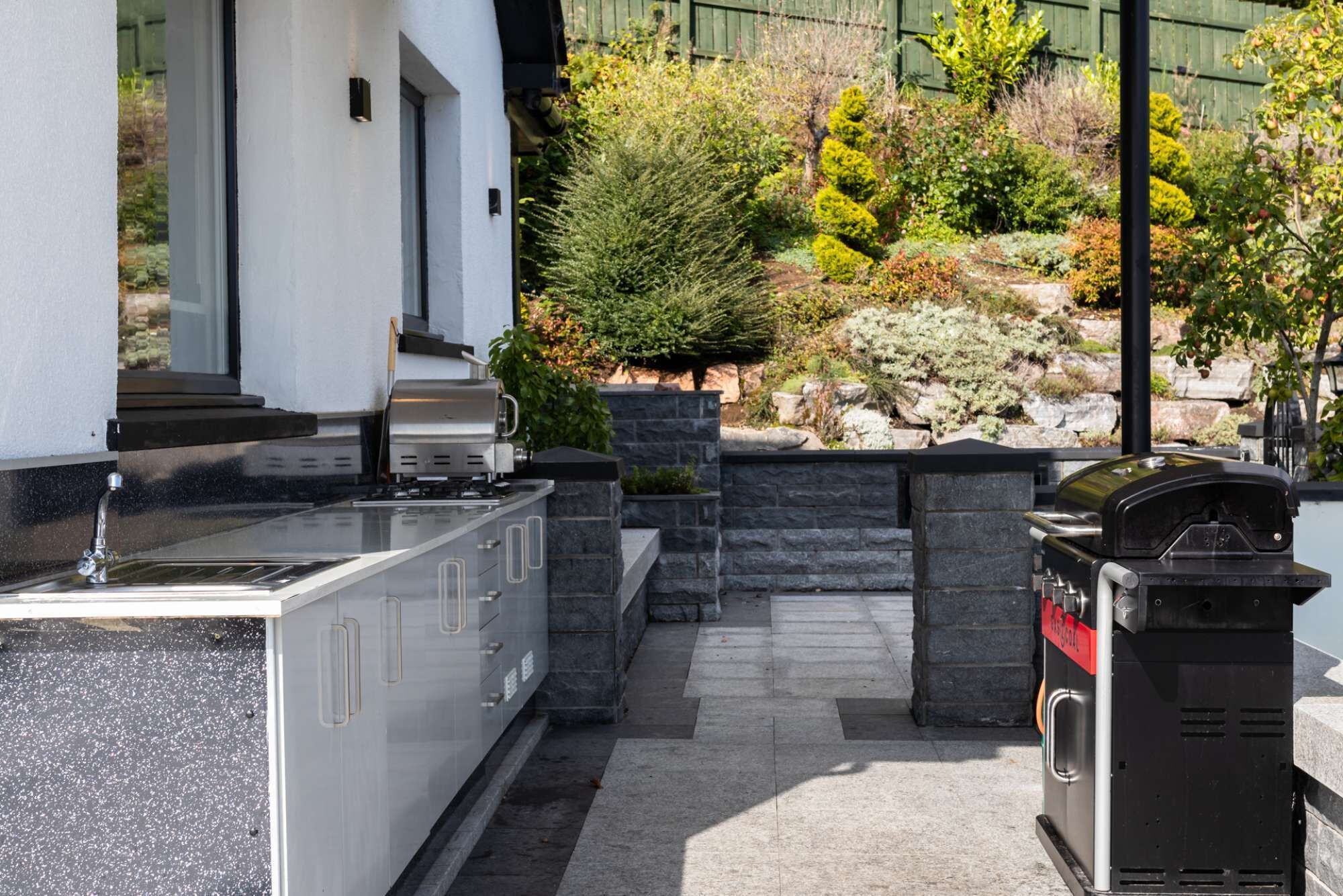 Eine Außenküche mit integriertem Spülbecken, Grill und Steinverzierungen.
